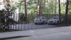 a car parked in front of a black fence with trees behind it on the sidewalk