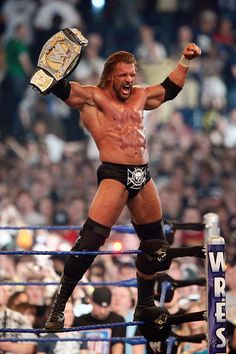 a man standing on top of a wrestling ring with his arms up in the air