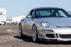 a silver sports car parked on top of a gravel field