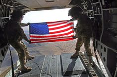 two soldiers holding an american flag in the back of a helicopter