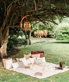 a blanket and pillows on the ground in front of a tree with chandelier hanging from it