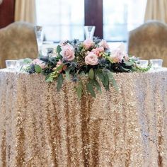 a gold sequin table cloth with pink flowers on it and greenery at the top