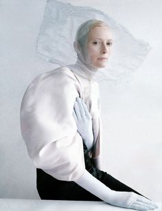 a woman with white hair and gloves on her head is sitting in front of a white background