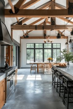 an open kitchen and dining room area with wooden beams on the ceiling, large windows in the background