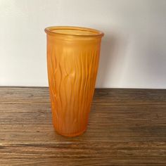 an orange glass sitting on top of a wooden table next to a white wall and wood floor