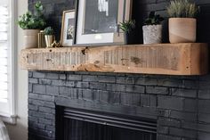 a black brick fireplace with potted plants on the mantle and framed pictures above it