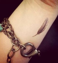 a wrist tattoo with a feather on it and a chain attached to the wrist that says love that it's so small but detailed