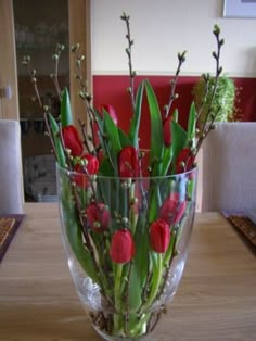 a vase filled with red flowers on top of a wooden table