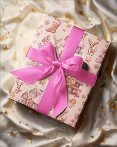 a pink gift box with a bow on top of white fabric and gold stars in the background