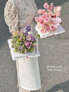 the woman is holding two trays with flowers in them on her hands and one has a bouquet