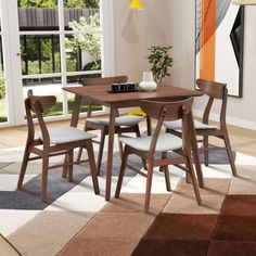 a dining table with four chairs in front of a large window and rug on the floor