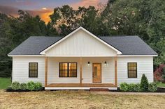 a small white house sitting on top of a grass covered field with trees in the background