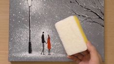 a person holding a sponge in front of a painting