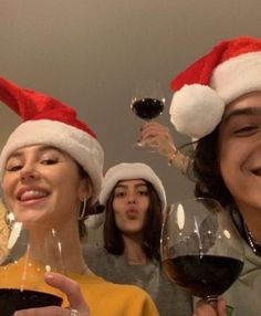 three people wearing santa hats and holding wine glasses in front of their faces, with one woman smiling at the camera