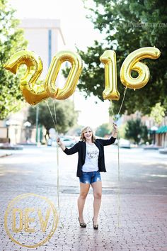 a woman holding two gold balloons in the shape of numbers, and standing on a brick road