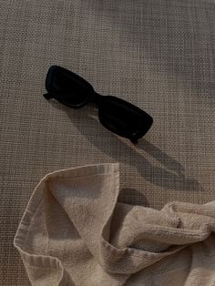 a pair of black sunglasses laying on top of a white cloth next to a piece of clothing