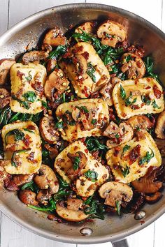 a pan filled with mushrooms and spinach on top of a wooden table