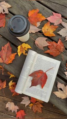 an open book with a leaf on it next to a cup of coffee and autumn leaves