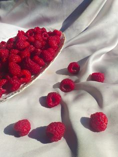 raspberries in a bowl on a white cloth with the sun shining through them