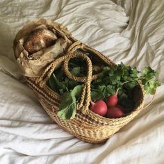 a wicker basket filled with vegetables on top of a white bed covered in sheets