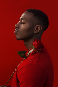 a young man with his eyes closed standing in front of a red wall and looking up