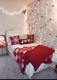 a bedroom decorated in red and white with christmas lights on the wall behind the bed