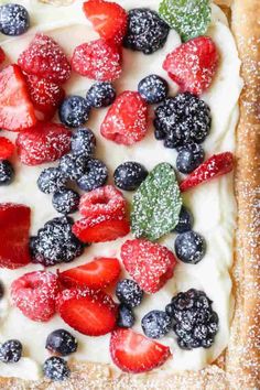 a pastry topped with berries and blueberries on top of a white cake sheet covered in powdered sugar