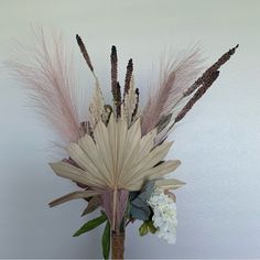 a vase filled with flowers and feathers on top of a wooden table next to a white wall