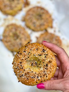 a hand holding a bagel with sesame seeds on it and other pastries in the background