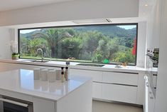 a kitchen with a large window that looks out onto the trees outside, and white counter tops