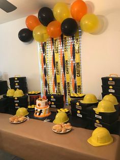 a table topped with yellow hard hats and desserts next to a balloon filled wall