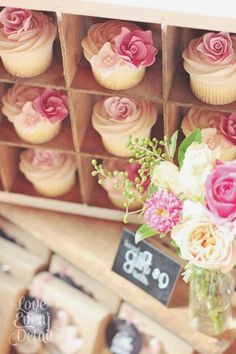 cupcakes with pink and white flowers are on display in a wooden box for sale