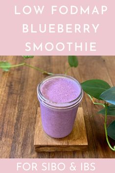 a jar of blueberry smoothie on top of a wooden table next to green leaves