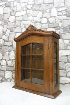 an old wooden cabinet with glass doors on the top and bottom, in front of a stone wall