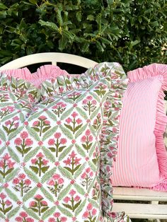 two pillows sitting on top of a white bench next to green trees and bushes with pink flowers