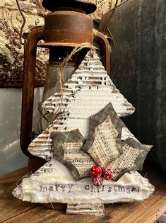 a christmas tree made out of old book pages on top of a wooden table next to a lantern