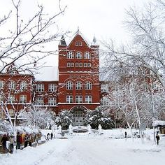 a large red brick building surrounded by snow covered trees and people walking in the street