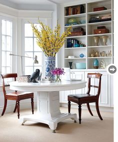 a white table with two chairs and a vase filled with flowers on top of it