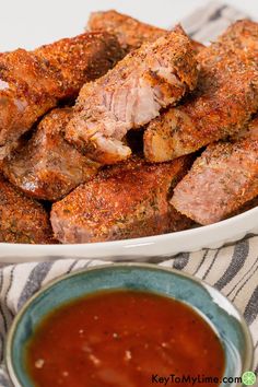 some meat is in a white bowl and sauce on a tablecloth next to it