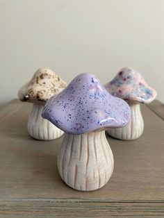 three small ceramic mushrooms sitting on top of a wooden table next to each other in different colors