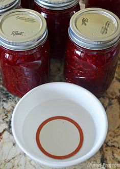 jars filled with red liquid sitting on top of a counter next to a white bowl