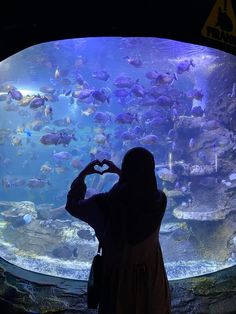 a woman is standing in front of an aquarium looking at fish and making a heart shape with her hands