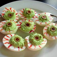 a white plate topped with devil's eggs and green toppings next to a black spider