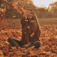 a woman is sitting in the leaves with her hands up to her face and eyes closed