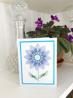 a blue and white flower card sitting on top of a table next to a potted plant