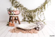 a stuffed animal laying on top of a wooden floor next to a basket filled with eggs and carrots