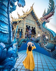 a woman wearing a yellow dress and hat standing in front of a building with dragon statues