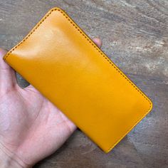 a hand holding a yellow wallet on top of a wooden table