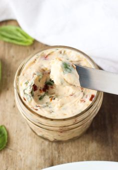 a spoon in a jar filled with food on top of a wooden table next to a plate