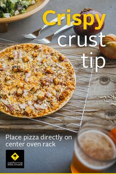 a pizza sitting on top of a wooden table next to a plate of food and drinks